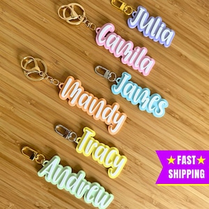 May include: Six colourful keychains with different names written in white on them. The names are: Julia, Camilla, James, Mandy, Tracy, and Andrew. The keychains are on a wooden surface.