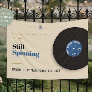May include: A cream-colored rectangular birthday banner featuring a large black vinyl record graphic on the right side. The text reads DELUXE 50TH BIRTHDAY EDITION, Still Spinning, and MARCUS · FIFTY YEARS YOUNG · EST. 1976. The record label says HAPPY BIRTHDAY MARCUS FIFTY '76.