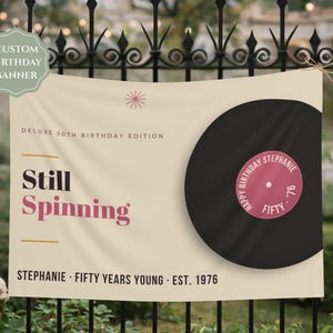 May include: A cream-colored rectangular birthday banner featuring a large black vinyl record graphic. Text reads: DELUXE 50TH BIRTHDAY EDITION, Still Spinning, STEPHANIE · FIFTY YEARS YOUNG · EST. 1976. The record label says: HAPPY BIRTHDAY STEPHANIE FIFTY '76.