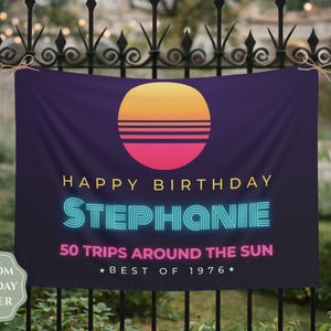 May include: A rectangular dark purple birthday banner featuring a sunset graphic with yellow, orange, and pink horizontal stripes. The text reads: HAPPY BIRTHDAY, STEPHANIE, 50 TRIPS AROUND THE SUN, and BEST OF 1976, with the name in a bright cyan neon style.