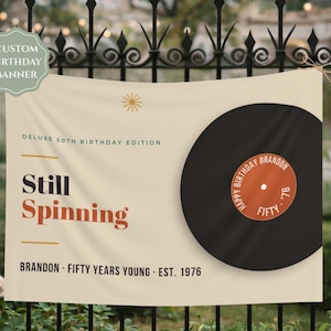 Op de afbeelding: Een crèmekleurige, rechthoekige verjaardagsbanner met een grote zwarte vinylplaat-afbeelding. De tekst luidt: CUSTOM BIRTHDAY BANNER, DELUXE 50TH BIRTHDAY EDITION, Still Spinning, BRANDON, FIFTY YEARS YOUNG, EST. 1976 en HAPPY BIRTHDAY BRANDON FIFTY '76.