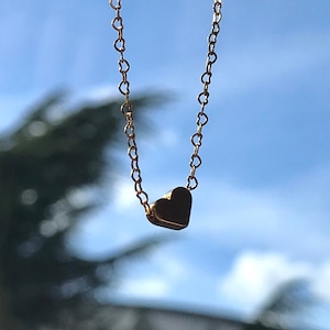 Gouden hart ketting van 18 k verguld goud met een achtergrond een boom en de lucht.De ketting heeft vormen van kleine hartjes en er is een gouden hart bedel die eraan hangt.