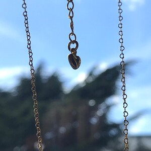 Een ketting verlenger hangt in de lucht met aan de uiteinde een klein goud hartje.Verder zie je de ketting met kleine vormen van harten.