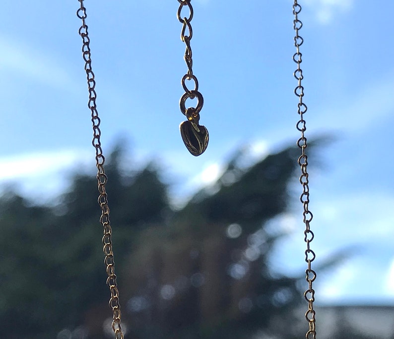 Een ketting verlenger hangt in de lucht met aan de uiteinde een klein goud hartje.Verder zie je de ketting met kleine vormen van harten.