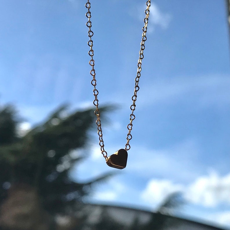 Gouden hart ketting van 18 k verguld goud met een achtergrond een boom en de lucht.De ketting heeft vormen van kleine hartjes en er is een gouden hart bedel die eraan hangt.