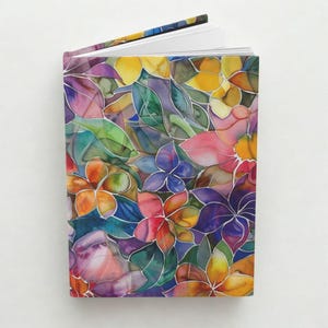 May include: An open journal with a colorful floral design. The cover features a vibrant pattern of flowers and leaves in shades of pink, purple, yellow, orange, and green. The pages are white, and the spine is visible.