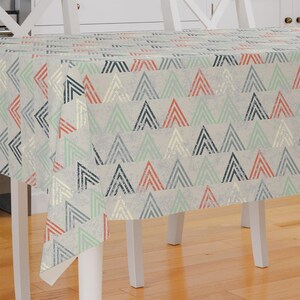 May include: A white tablecloth with a geometric pattern of gray, red, and green triangles. The tablecloth has a distressed, vintage look.