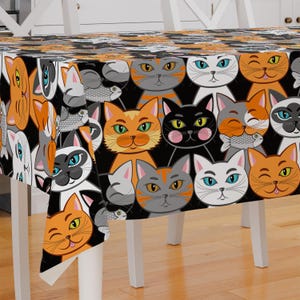May include: Black tablecloth with a repeating pattern of colorful cartoon cats with different expressions. The cats are wearing various colors and patterns, including orange, gray, black, and white. Some cats are holding fish.