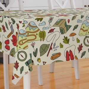 May include: A cream-colored tablecloth with a whimsical camping-themed pattern. The design features mountains, trees, compasses, binoculars, and other outdoor adventure icons in a variety of colors.