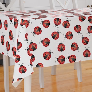 May include: White tablecloth with a repeating pattern of red ladybugs. The ladybugs have black spots and are arranged in a staggered pattern.