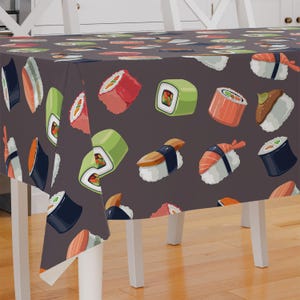 May include: A dark gray tablecloth with a repeating pattern of colorful sushi rolls. The tablecloth is made of a soft, durable fabric and is perfect for adding a fun and festive touch to any dining table.
