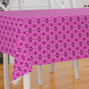 May include: Pink tablecloth with a geometric pattern of overlapping squares and diamonds. The tablecloth is draped over a white table with white chairs.
