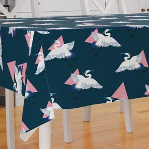 May include: A dark blue tablecloth with a repeating pattern of white birds and pink triangles. The tablecloth is draped over a white table with white legs.