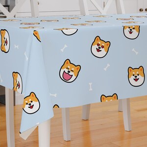 Peut inclure: Une nappe bleu clair avec un motif répété de visages de chiens Shiba Inu souriants et de formes d'os blancs.