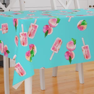 May include: A turquoise tablecloth with a repeating pattern of pink ice lollies and peaches. The tablecloth is laid out on a wooden table.
