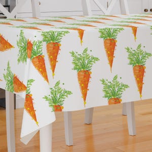 May include: White tablecloth with a repeating pattern of orange carrots with green tops. The tablecloth is on a white table with wooden legs.