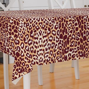 May include: A brown and beige leopard print tablecloth with a white background. The tablecloth is draped over a white table with four legs.