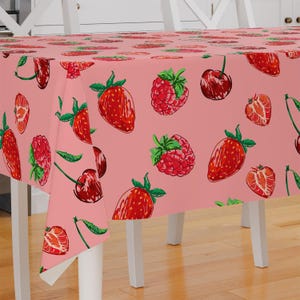 Puede incluir: Mantel de mesa rosa con un patrón repetido de fresas, frambuesas y cerezas. El mantel está hecho de una tela suave y duradera, ideal para el uso diario.