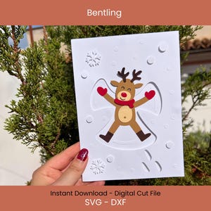 May include: A white card featuring a reindeer making a snow angel, with a red scarf and mittens. The card has a snowflake design and the text "Bentling" at the top. The bottom of the card reads "Instant Download - Digital Cut File SVG - DXF".