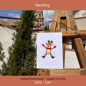 May include: A white card featuring a reindeer angel design with a red scarf and mittens, surrounded by snowflakes. The card is displayed on a wooden structure with the text "Bentling" at the top and "Instant Download - Digital Cut File SVG - DXF" at the bottom.