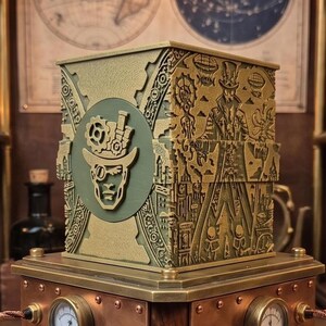 May include: A steampunk-themed box with intricate brass and copper detailing. The box features a circular emblem with a figure wearing goggles and a top hat. The base has gauges and glowing tubes, with a small robot in the background.