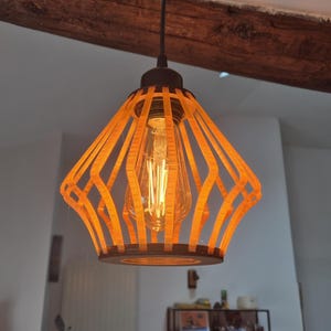 Puede incluir: Una lámpara colgante de madera con un diseño geométrico. La luz está hecha de finas tiras de madera que están dispuestas en un patrón de diamante. La luz está encendida y la bombilla brilla.