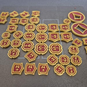 Könnte beinhalten: Eine Sammlung gelb-roter Spielmarken mit verschiedenen Zahlen und Symbolen. Die Marken haben unterschiedliche Formen, darunter Schilde und Kreise. Einige Marken zeigen die Zahlen +4, -5 und +5.