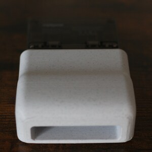 May include: A white plastic case with a rectangular opening. The case is designed to hold a small electronic device.