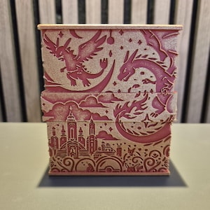 Peut inclure: Une bo&icirc;te rectangulaire rose avec des motifs d&eacute;coup&eacute;s au laser. La bo&icirc;te pr&eacute;sente des dragons, des &eacute;toiles et un paysage urbain. Le design est d&eacute;taill&eacute; et la bo&icirc;te semble &ecirc;tre en bois ou dans un mat&eacute;riau similaire. Le th&egrave;me g&eacute;n&eacute;ral est la fantaisie.