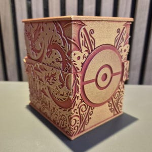 Peut inclure: Bo&icirc;te d&eacute;corative &agrave; couvercle articul&eacute;, avec des motifs d&eacute;coup&eacute;s au laser en or et rouge. La bo&icirc;te pr&eacute;sente un embl&egrave;me circulaire pro&eacute;minent avec un point central, entour&eacute; de motifs orn&eacute;s et de motifs de dragons. La bo&icirc;te est en bois.