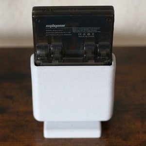 May include: A white charging stand with a black battery charger for a Mipow Power Bank. The charger has the text "Mipow" and "MODEL: M3YPOWER" on it. The charger is plugged into the stand and is ready to charge.