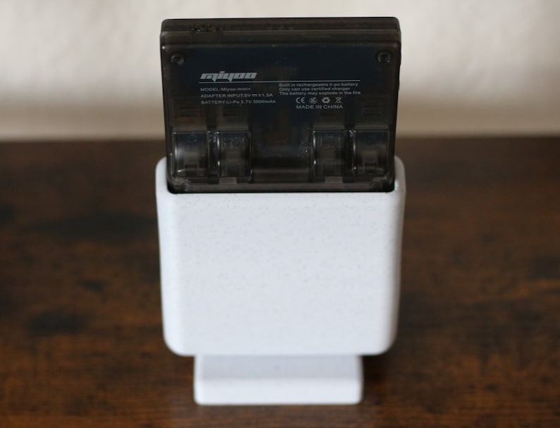 May include: A white charging stand with a black battery charger for a Mipow Power Bank. The charger has the text "Mipow" and "MODEL: M3YPOWER" on it. The charger is plugged into the stand and is ready to charge.