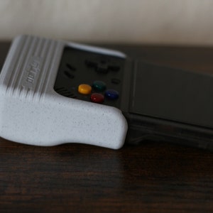 May include: A white handheld gaming console with a black screen and a multi-colored button pad. The console has a textured surface and the word "retro" printed on the side.