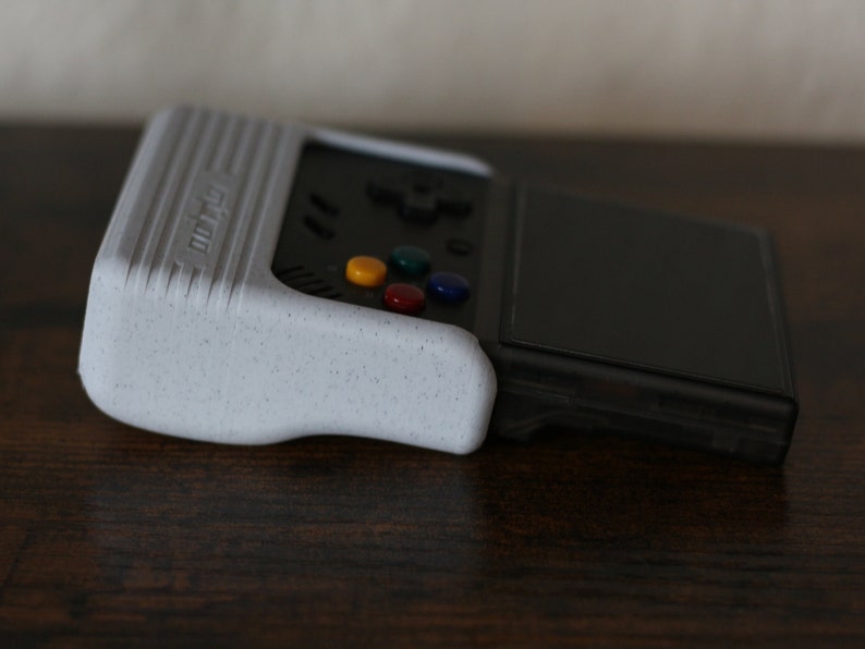 May include: A white handheld gaming console with a black screen and a multi-colored button pad. The console has a textured surface and the word "retro" printed on the side.