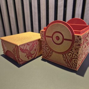 Peut inclure: Deux bo&icirc;tes d&eacute;coratives rouges et dor&eacute;es. L'une est rectangulaire avec un couvercle dor&eacute; scintillant et un motif de ph&eacute;nix rouge. L'autre est une bo&icirc;te carr&eacute;e avec un motif circulaire et une palette de couleurs rouge et or. Les bo&icirc;tes ont des motifs complexes.