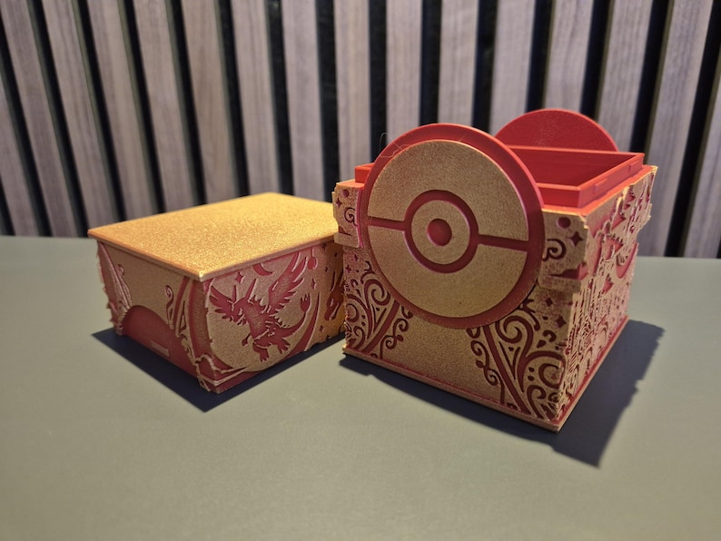 Peut inclure: Deux bo&icirc;tes d&eacute;coratives rouges et dor&eacute;es. L'une est rectangulaire avec un couvercle dor&eacute; scintillant et un motif de ph&eacute;nix rouge. L'autre est une bo&icirc;te carr&eacute;e avec un motif circulaire et une palette de couleurs rouge et or. Les bo&icirc;tes ont des motifs complexes.