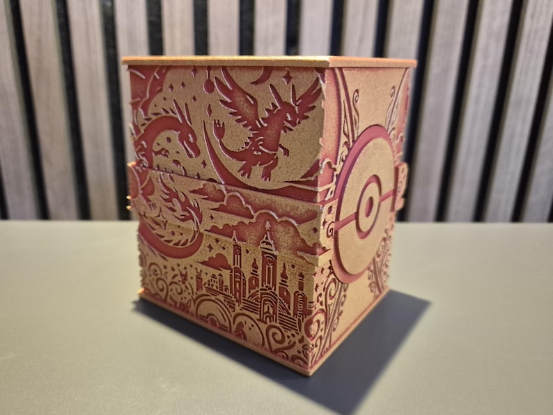 Peut inclure: Une bo&icirc;te d&eacute;corative avec des motifs d&eacute;coup&eacute;s au laser complexes. La bo&icirc;te pr&eacute;sente une palette de couleurs rouge et or, avec des illustrations de dragons, d'une ville et d'un embl&egrave;me circulaire. La bo&icirc;te est rectangulaire et poss&egrave;de un couvercle &agrave; charni&egrave;re.