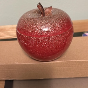 May include: A red apple-shaped trinket box with a gold glitter finish and a brown stem.