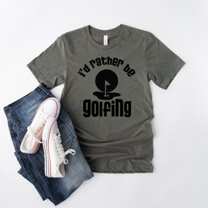 May include: A green t-shirt with the text "I'd rather be golfing" in black. The text is in a retro font and includes a black silhouette of a golf ball with a flag in a hole.