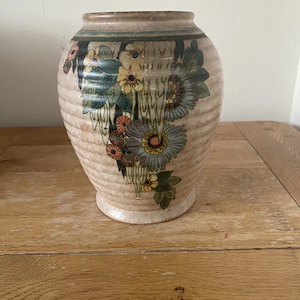 May include: A ceramic vase with a floral design. The vase is white with brown, green, yellow, and blue flowers.