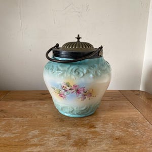 May include: A vintage blue and white ceramic biscuit jar with a floral design and a silver-toned lid with a handle.