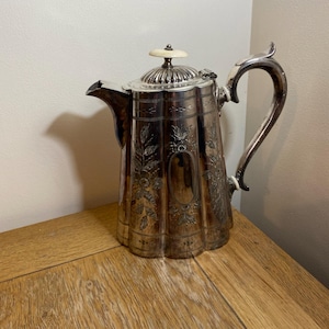 May include: A silver teapot with an ornate floral design and a white knob on the lid.