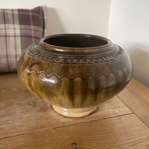May include: A brown ceramic pot with a wavy rim and a light brown base. The pot has a glazed finish and a subtle brown and green colour variation.
