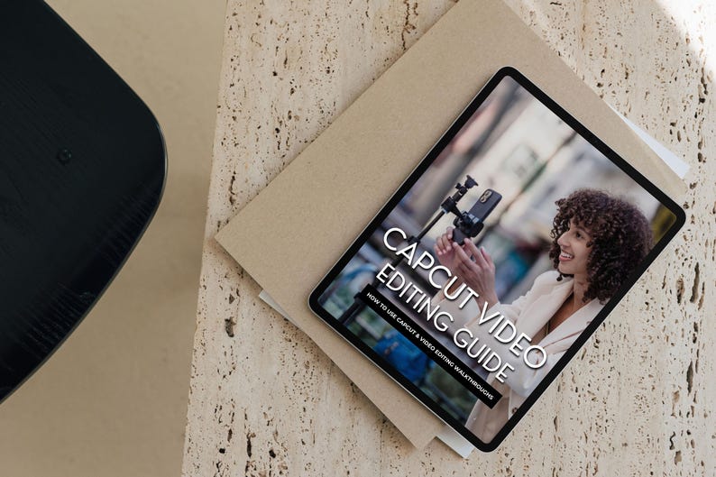 May include: A tablet displaying a guide on how to use CapCut for video editing. The guide is titled "CapCut Video Editing Guide: How to Use CapCut & Video Editing Walkthroughs". The image shows a person holding a smartphone and a tripod.