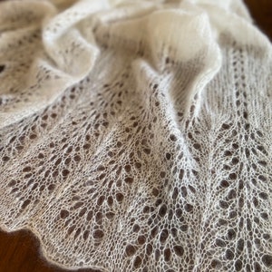 Elbert scarf is a hand-knitted lace shawl with a fine, lightweight mohair/silk blend. The airy, free flowing knitted pattern creates a delicate yet effortless elegance, perfect for draping over the shoulders. With its scalloped edges and soft halo, this shawl is an ideal choice for special occasions, bridal wear, or as a timeless, handmade accessory. Its flowing design and lightweight feel make it a beautifully simple yet sophisticated piece.