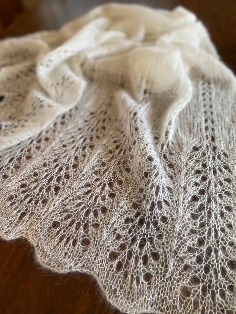 Elbert scarf is a hand-knitted lace shawl with a fine, lightweight mohair/silk blend. The airy, free flowing knitted pattern creates a delicate yet effortless elegance, perfect for draping over the shoulders. With its scalloped edges and soft halo, this shawl is an ideal choice for special occasions, bridal wear, or as a timeless, handmade accessory. Its flowing design and lightweight feel make it a beautifully simple yet sophisticated piece.
