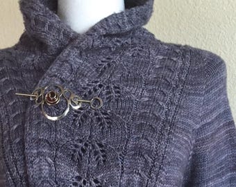 May include: A gray knitted cardigan with a hood and a silver brooch with a brown stone.