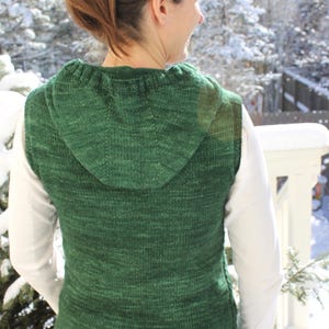May include: A green hooded sleeveless sweater with a textured knit pattern. The sweater is made of a soft, warm material and is perfect for layering.