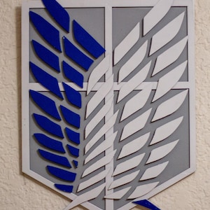 May include: A wooden emblem with a shield shape, featuring blue and white wings on a grey background. The emblem has a white border and is mounted on a textured wall. The design is a stylized representation of wings.