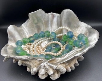 May include: A silver clam shell dish filled with green and blue glass beads and a white pearl necklace.